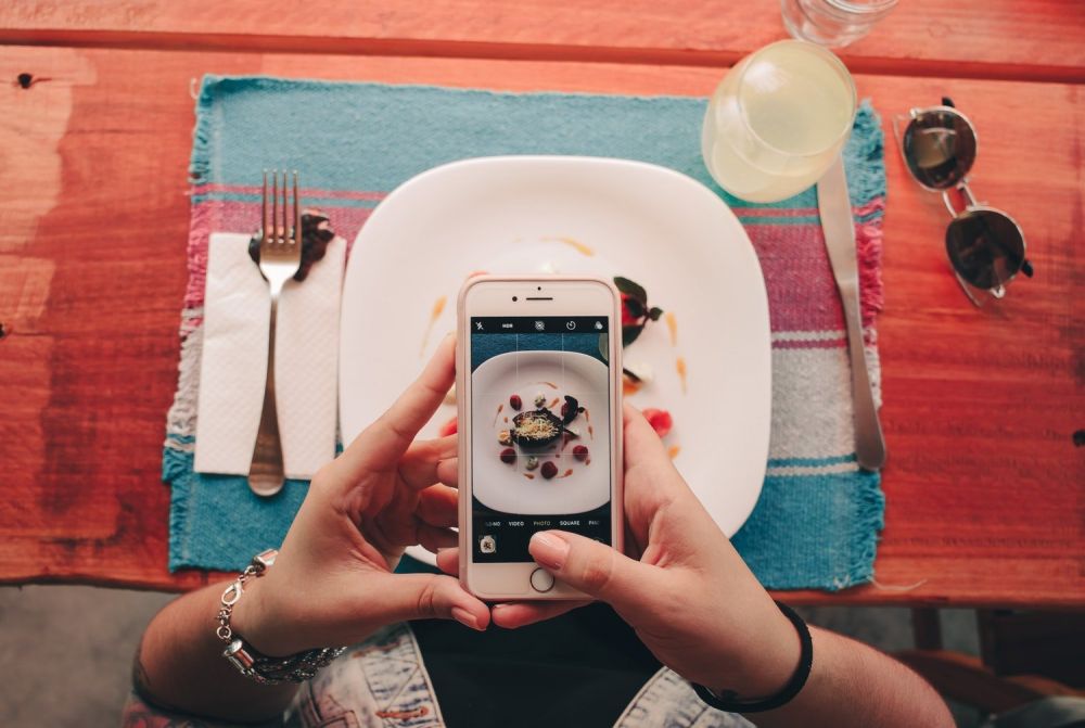 Persona che fotografa cibo in un ristorante con il cellulare, foto di Victor Freitas da Pexels