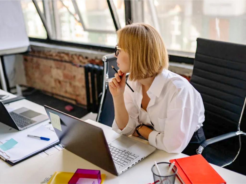 donna che pensa davanti ad una scrivania piena di cose da fare